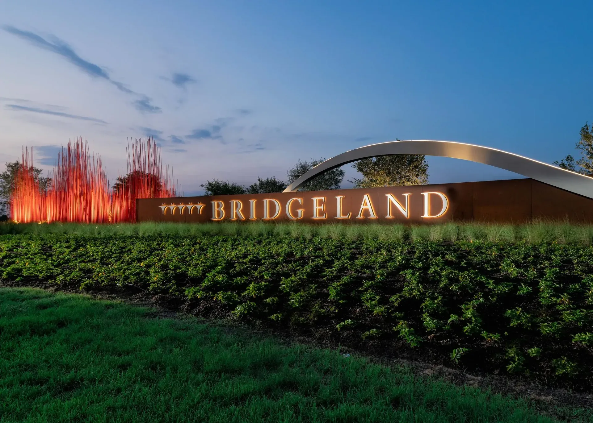 Bridgeland entrance monument at dusk with the steel arch and light installation