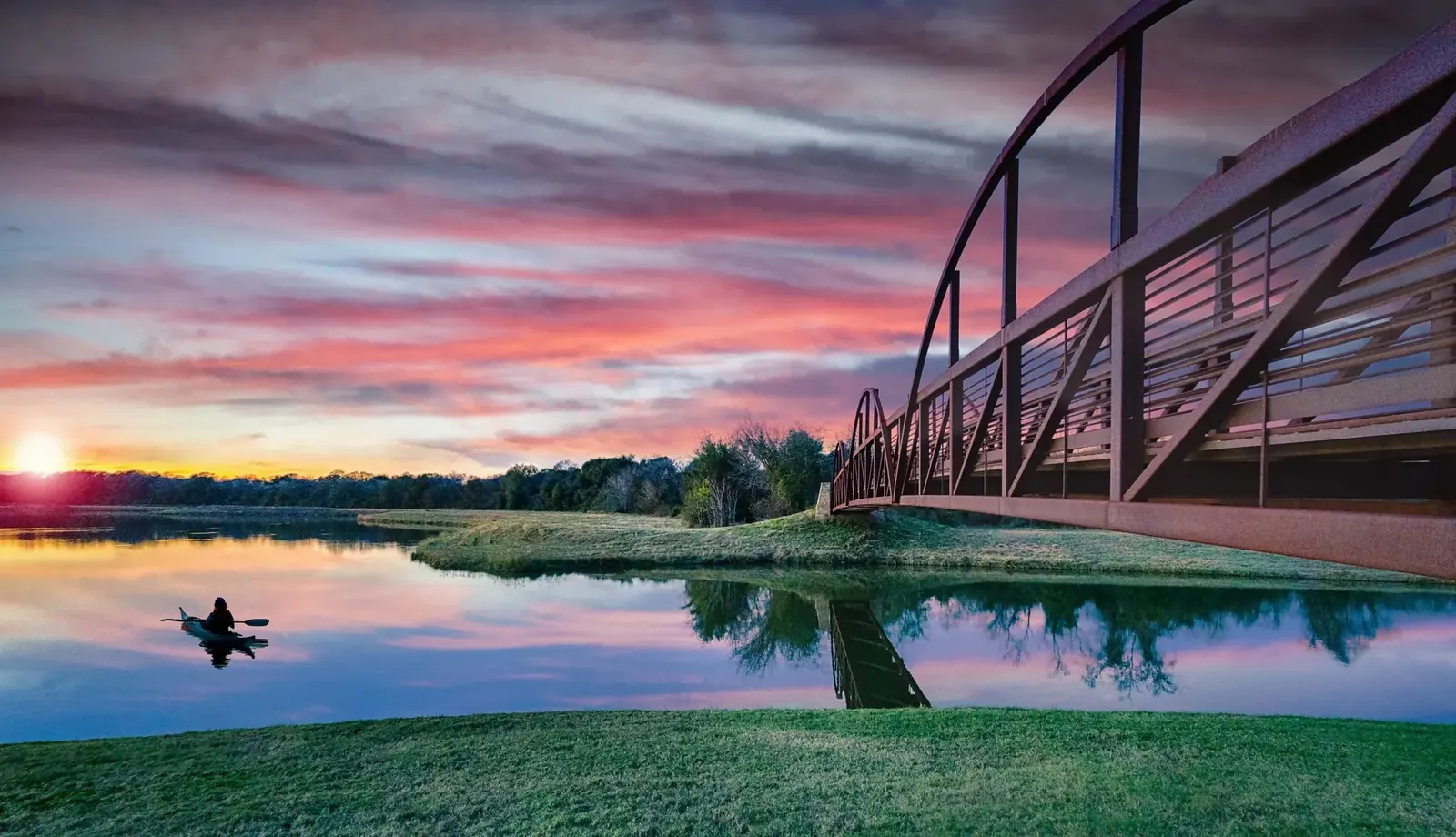 Kayaker on still water at sunset beneath the arched steel pedestrian bridge, Bridgeland
