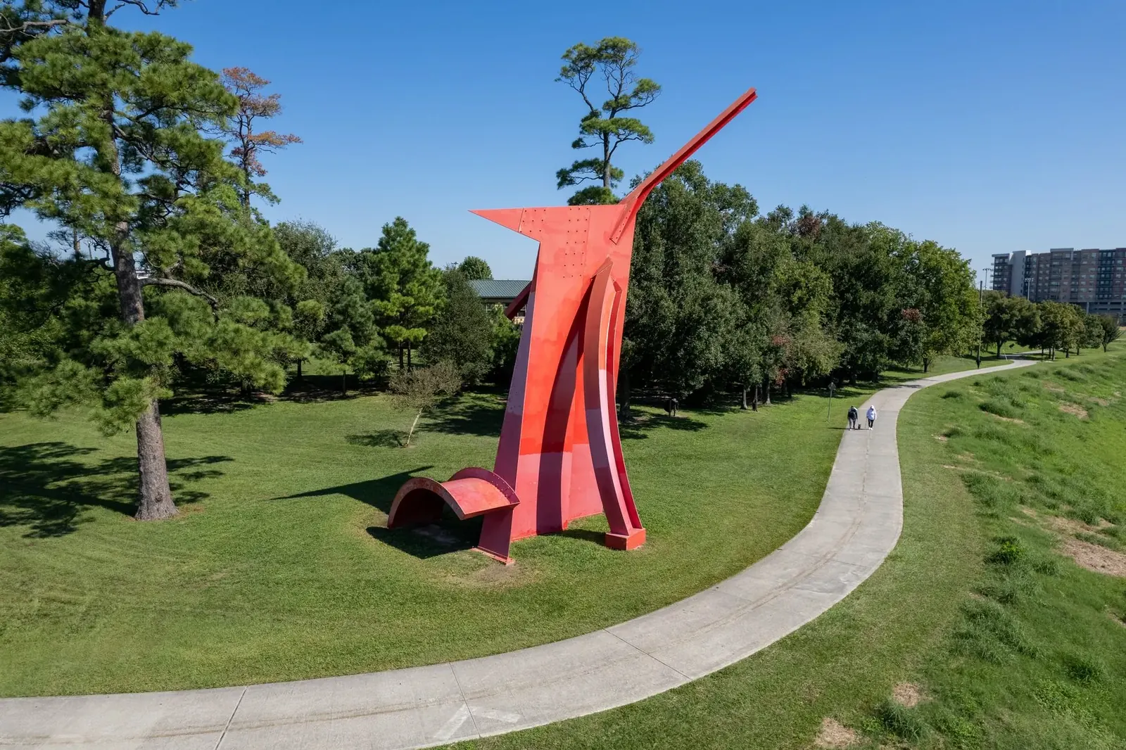 Red abstract sculpture beside a curving greenway trail