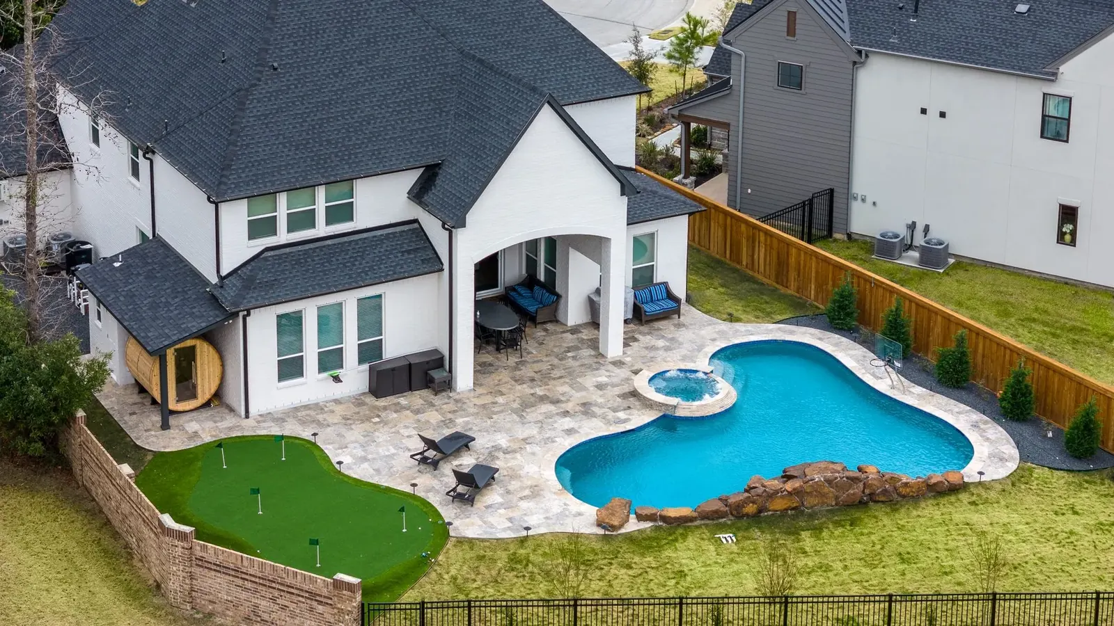 Drone view of a backyard pool, spa, putting green, and covered patio