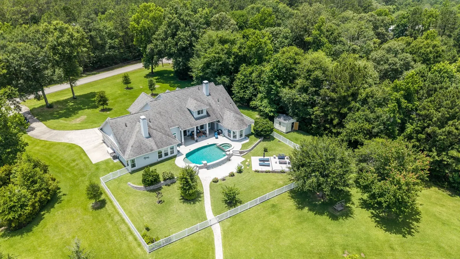 Aerial of a wooded estate with pool, white fence, and circular drive