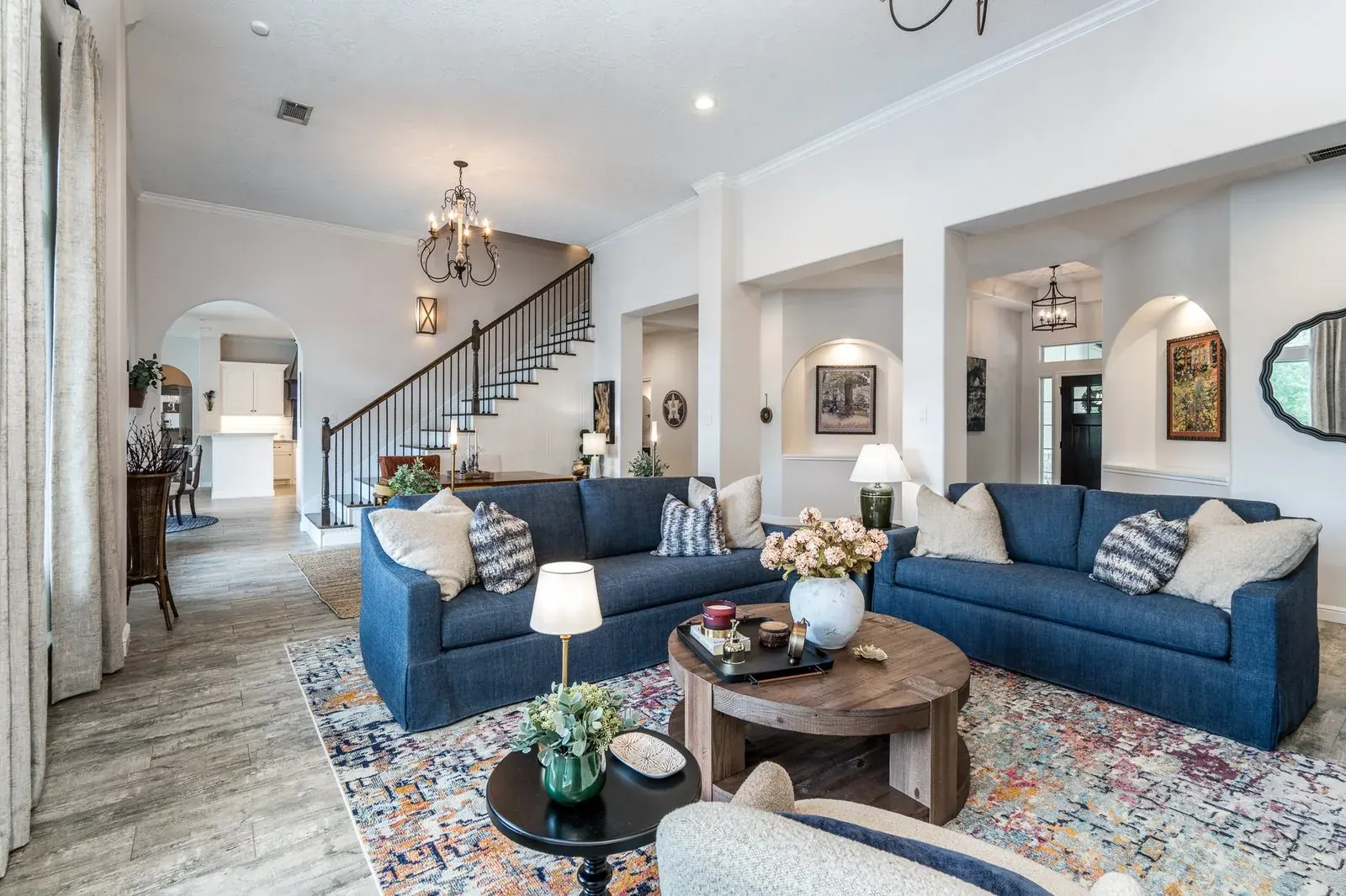 Staged living room with navy sofas, wood tables, and a staircase beyond