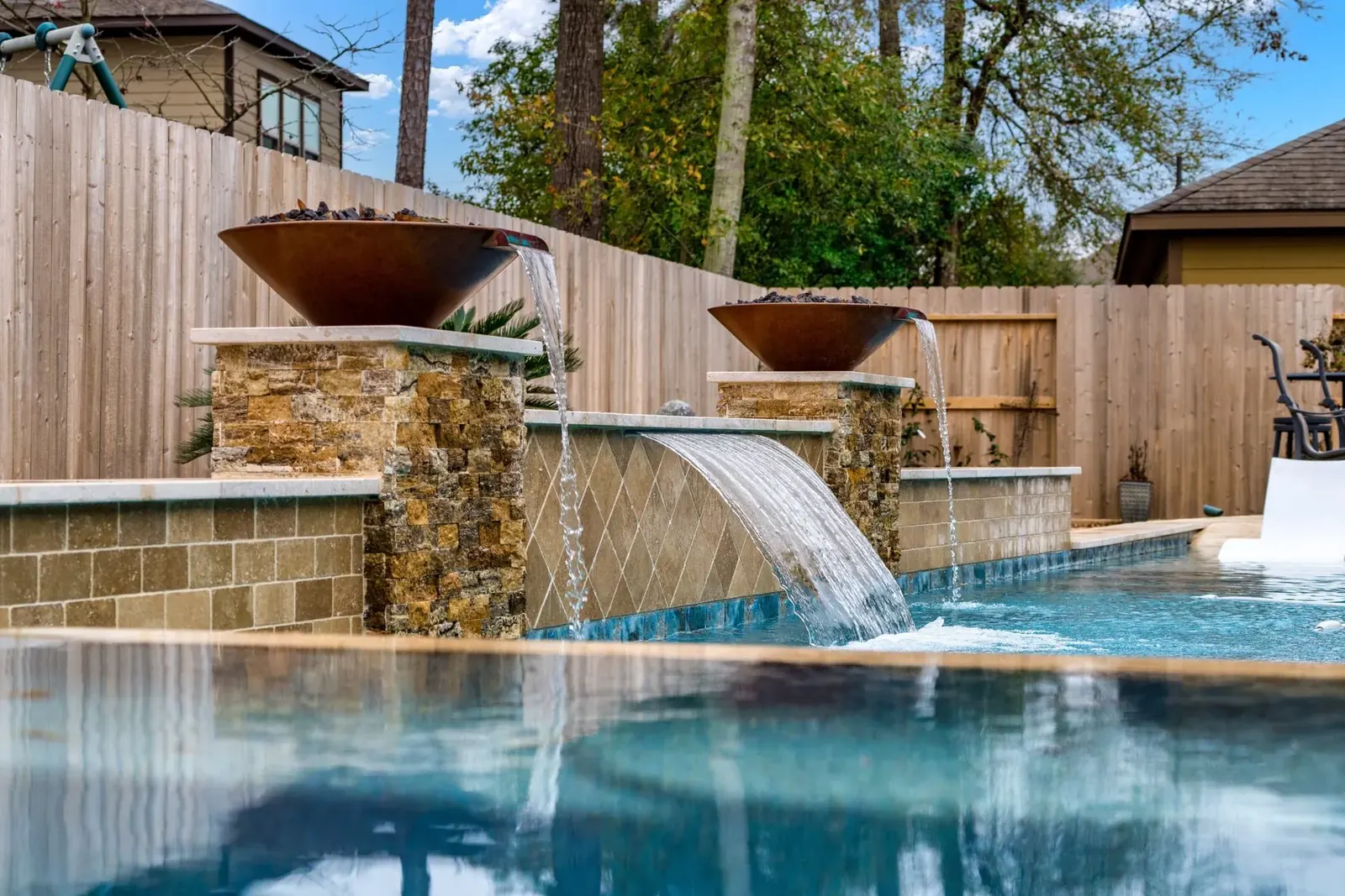 Copper fire bowls spilling water into a pool over stacked stone