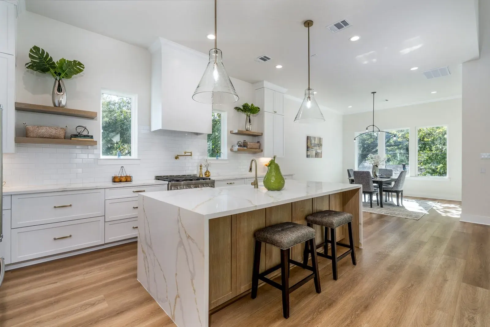 Bright white kitchen with marble island, glass pendants, and brass fixtures